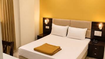 A hotel room with a large bed, bedside tables, an air conditioning unit, and a ceiling fan.