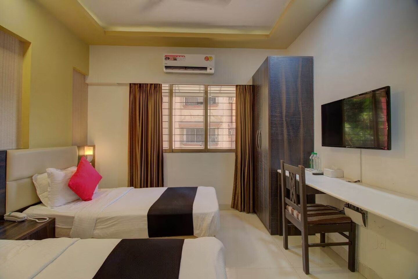 Une chambre d’hôtel avec deux lits, un bureau, une chaise, un climatiseur, une télévision et une fenêtre avec des rideaux.