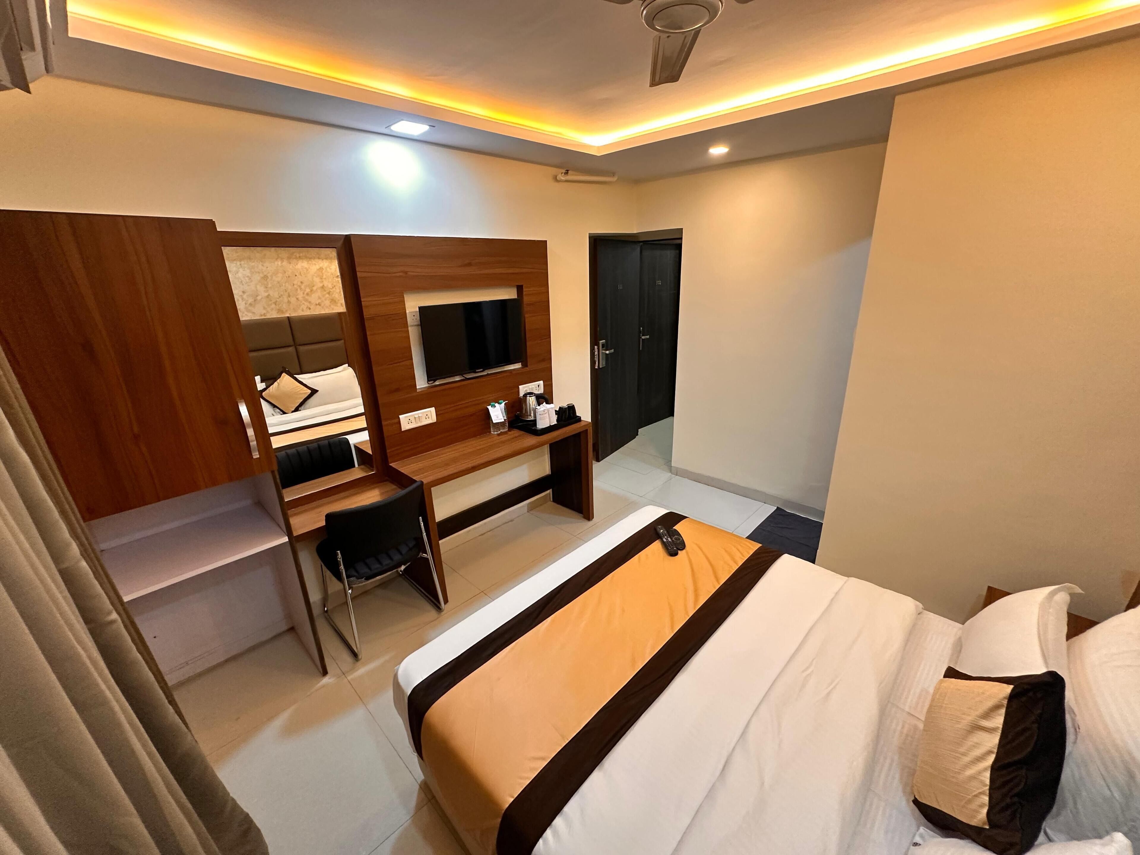 A hotel room with a bed, a desk, a chair, a TV, and a door.