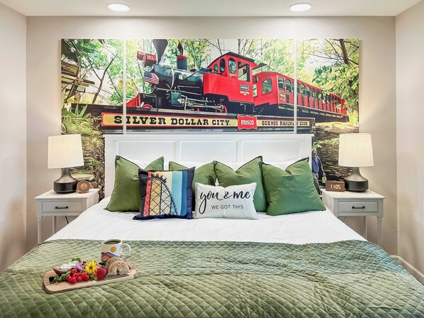 A bedroom with a bed, pillows, a bedside table with a lamp, a tray with food, and a wall mural of a train. - Patio on Pointe Royale Golf Course, Pools, Updated (Branson)