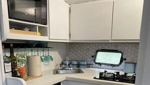 A compact kitchen with a microwave, sink, and dishwasher, featuring white cabinets and a hexagonal backsplash. - My Time Boat House, Coconut Grove Miami (Miami)