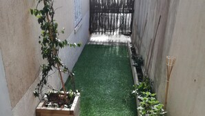 Een smalle binnentuin met kunstgras, een houten plantenbak en een bamboiraak.