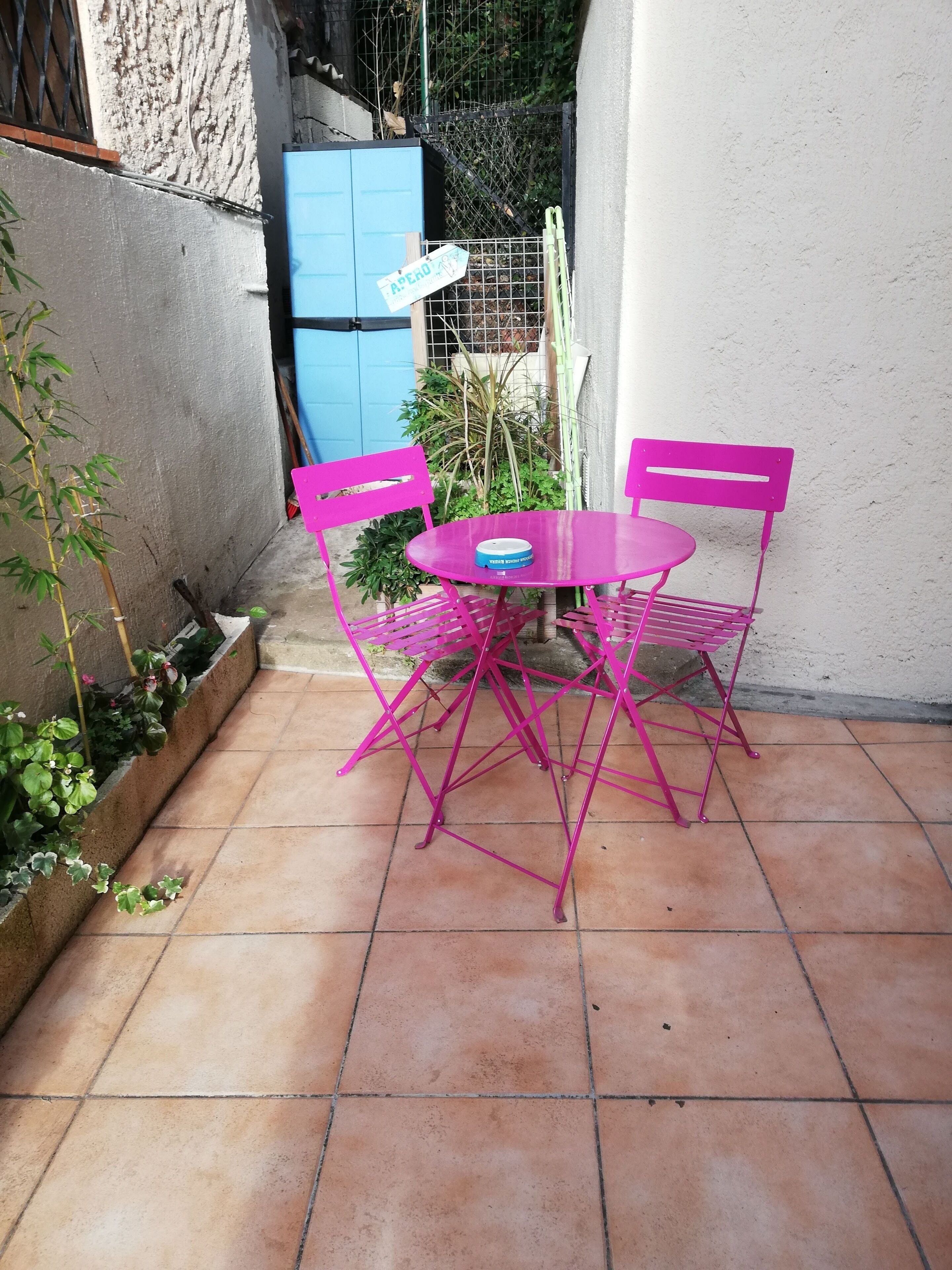 A small patio with a round table and two chairs, surrounded by a low brick wall and a small garden.