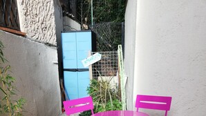 Een klein terras met een ronde tafel en twee stoelen, omgeven door een lage bakstenen muur en een kleine tuin.