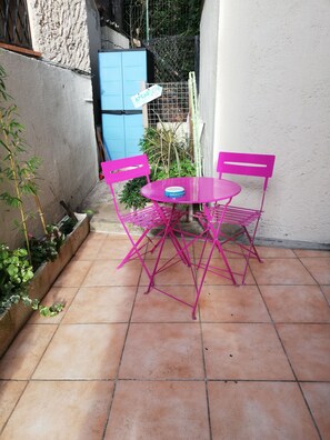A small patio with a round table and two chairs, surrounded by a low brick wall and a small garden. - Studio with sleeping area 15 min walk from the Croisette (Cannes)