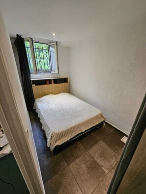 A small bedroom with a bed, a window, and a door. - Studio with sleeping area 15 min walk from the Croisette (Cannes)