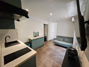 A compact kitchen with a sink, stove, and a small countertop. There is a light-colored tiled floor and a sofa in the adjacent living area. - Studio with sleeping area 15 min walk from the Croisette (Cannes)