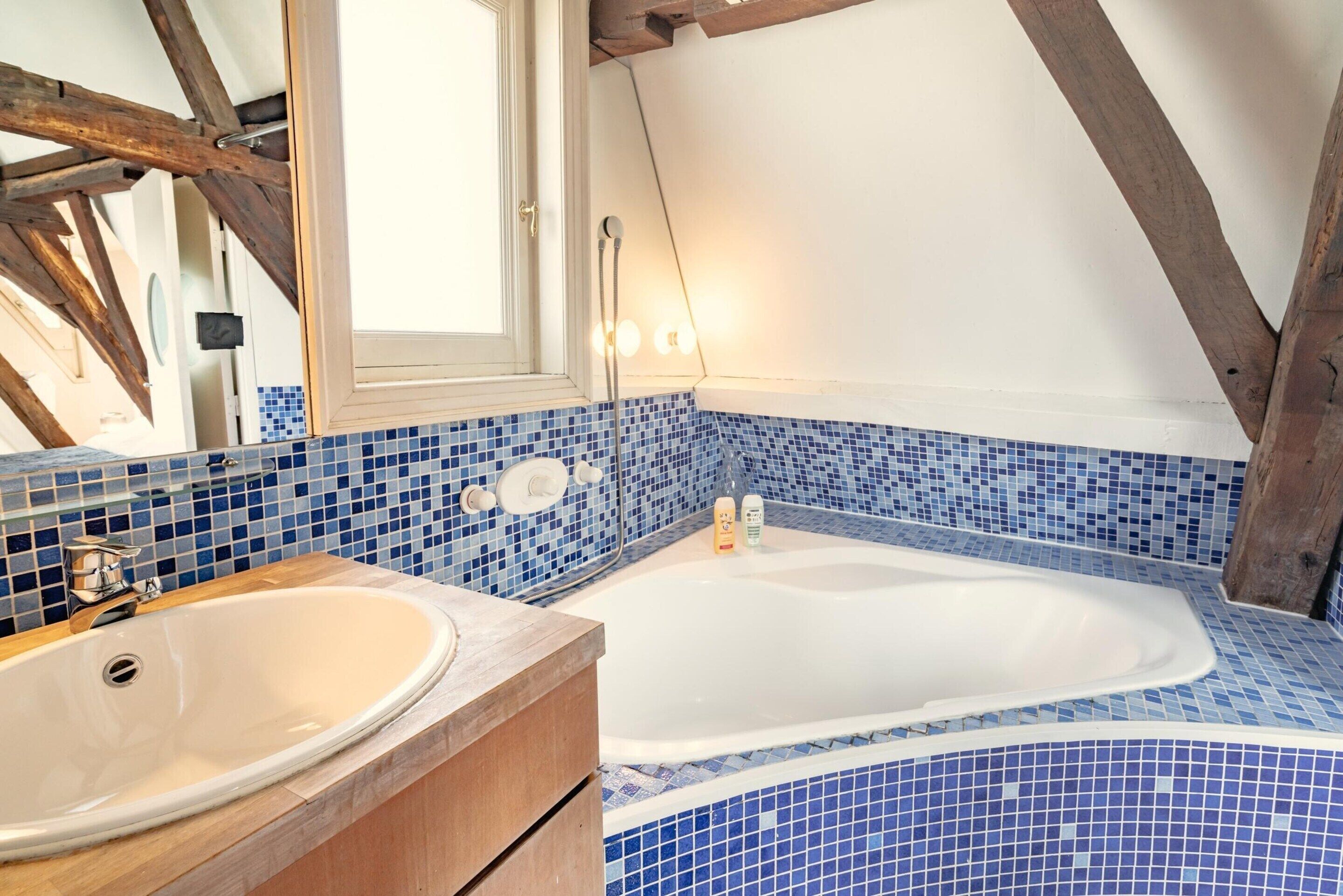 A bathroom with a bathtub, a sink, and blue-tiled walls.