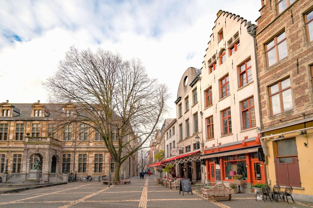 A cobblestone street lined with historic buildings, a statue, and outdoor seating areas.