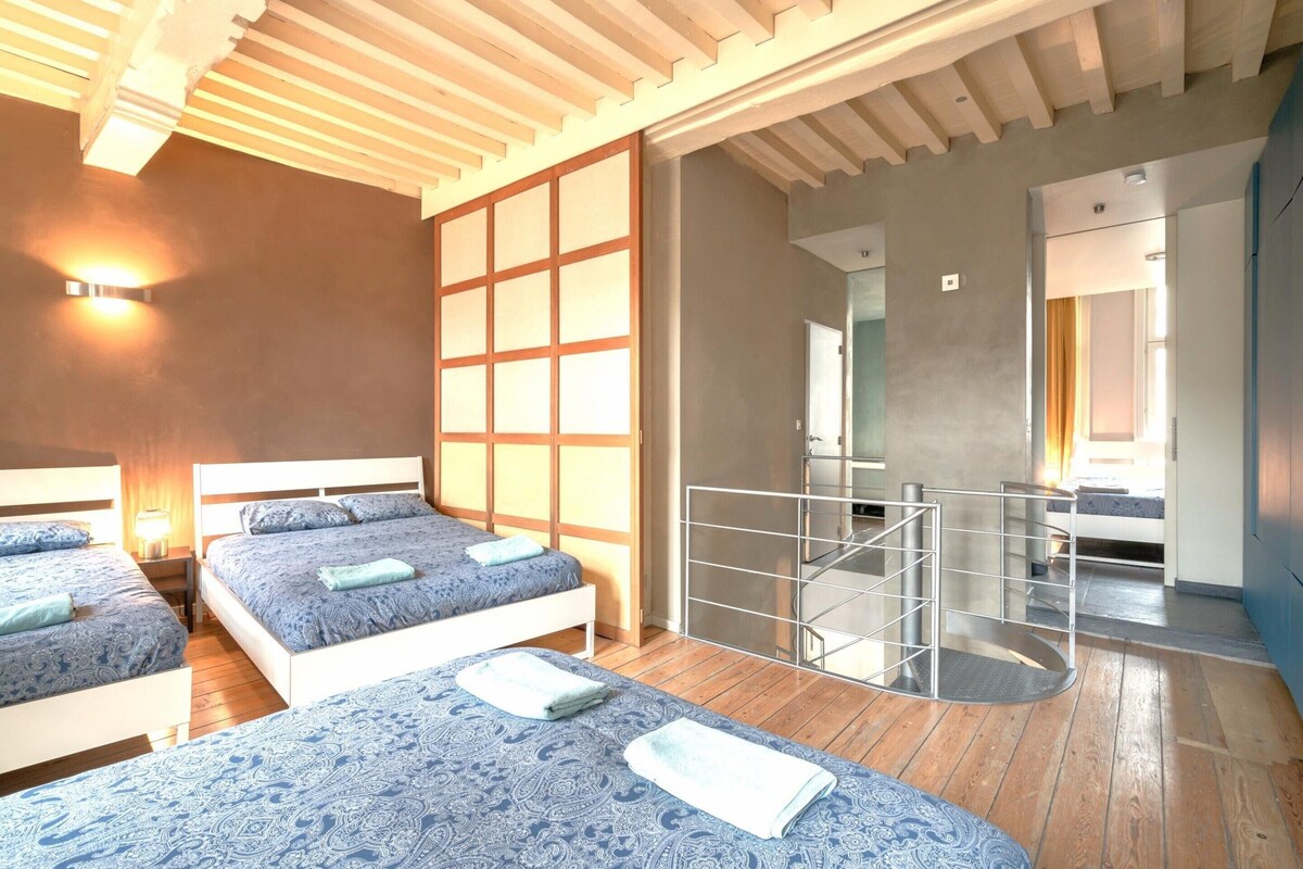Une chambre d’hôtel avec deux lits, un plafond en bois, une porte coulissante et un balcon doté d’une rambarde en métal.