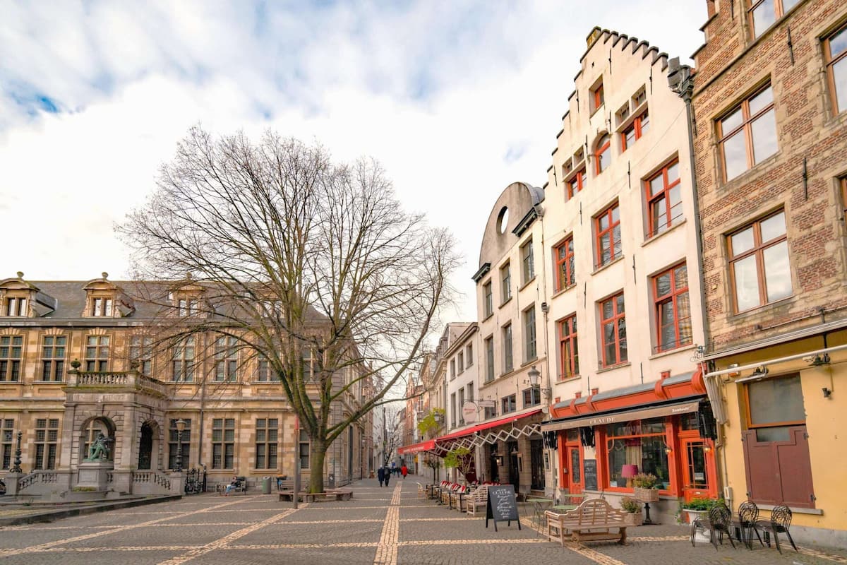 Una calle empedrada flanqueada por edificios históricos, una estatua y zonas de estar al aire libre.