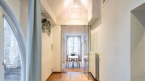 Un couloir doté d’un plancher en bois, un coin repas avec une table et des chaises, et une grande fenêtre avec des rideaux.