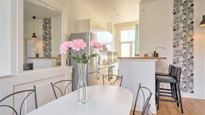 Une cuisine moderne avec des meubles blancs, un réfrigérateur en acier inoxydable et un coin repas comprenant une table et des chaises blanches.