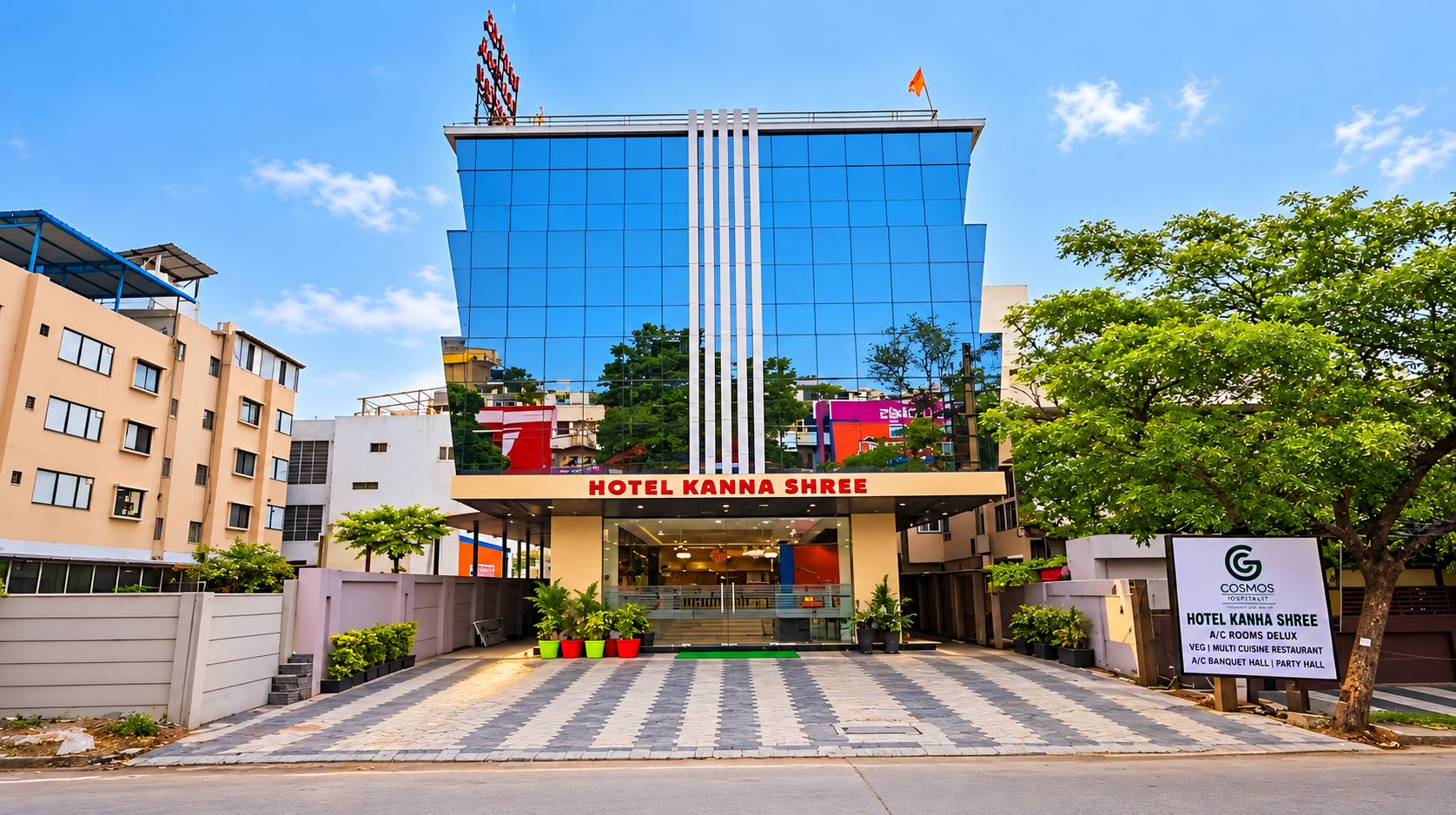 A modern hotel building with a prominent entrance, a flag on top, and a sign indicating it is a Cosmos Hospital Hotel.
