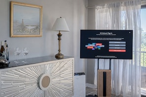 Habitació d'hotel moderna amb un televisor de pantalla plana que mostra la pantalla d'inici de sessió de LG, una làmpada decorativa, una obra d'art emmarcada i vista a l'exterior a través de cortines translúcides.
