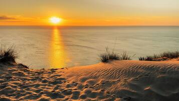 Un paysage désertique avec des dunes de sable et un coucher de soleil sur l’océan.