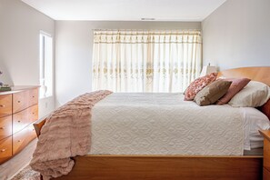 Un dormitorio con una cama de madera, una mesita de noche, un aparador y una ventana con cortinas.