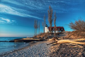 A coastal scene with a lighthouse, a red-roofed building, and a rocky shoreline. - Stunning Condo, in Williamsburg with designer furnishing and breathtaking view (Traverse City)