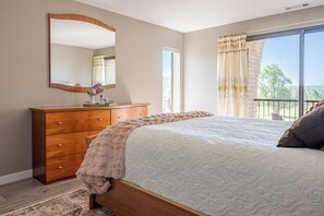 A bedroom with a bed, dresser, mirror, and a view of the outdoors.