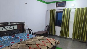 A bedroom with a bed, a chair, a table, and curtains. - rk tourist loge (Ukhimath)