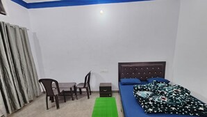 A bedroom with a bed, a desk, two chairs, a green rug, and a window with curtains. - rk tourist loge (Ukhimath)