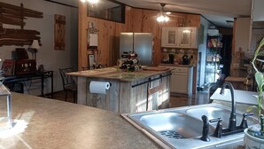 A kitchen with wooden cabinets, a central island with a sink, and a ceiling fan. - Relaxing Beautiful Views Plenty of Back Roads to Ride ATVs-Horses- Pets Welcomed (Aiken)
