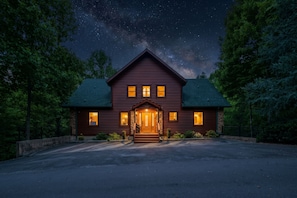 A two-story log cabin with a prominent front entrance, illuminated windows, and a driveway leading to the entrance. - Sleeps 10, King Suite in Every Bedroom, Hot Tub, 5.9 Mi to Downtown Gatlinburg (Gatlinburg)
