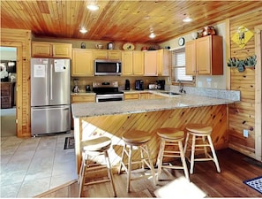 A kitchen with wooden cabinets, stainless steel appliances, a granite countertop, and a bar area with stools. - Majestic Views, Hot Tub, and Game room (Gatlinburg)