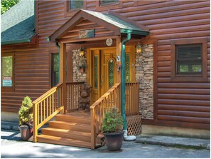 A log cabin with a wooden porch, a stone wall, and a mailbox. - Majestic Views, Hot Tub, and Game room (Gatlinburg)