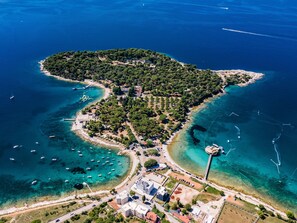 An aerial view of a coastal town with clear blue waters, a small island with dense greenery, and a few buildings near the shore. - Villa Elite 1 by Interhome (Pula)