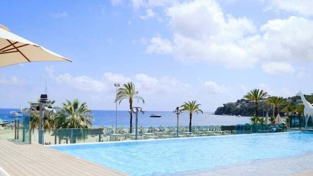 Ein Poolbereich mit Blick auf das Meer, Palmen und eine entfernte Insel.