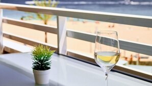 Ein Balkon mit Glastisch, einem Weinglas mit Weißwein und einem kleinen Topfpflanzen.