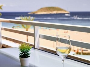 Ein Balkon mit Glastisch, einem Weinglas mit Weißwein und einem kleinen Topfpflanzen.