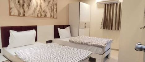A modern bedroom with two beds, a large abstract painting, a ceiling light, and a built-in air conditioning unit.