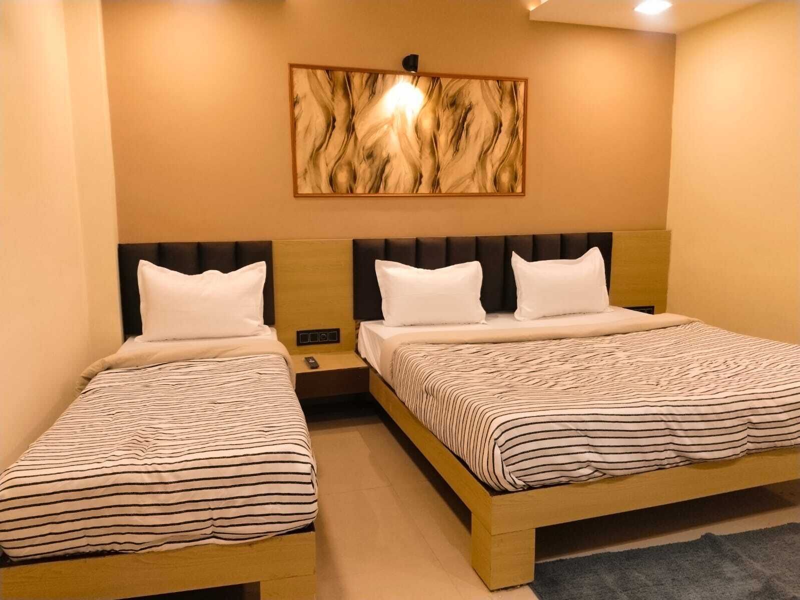 Hotellihuone, jossa on kaksi sänkyä, sängynpääty, jossa on valaisin, ja seinälle kiinnitetty taideteos.