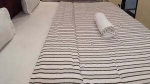 A hotel room with a large bed, a smaller bed, a ceiling fan, an air conditioning unit, a flat-screen TV, and a large abstract painting on the wall. - Lalji S Hotel And Restaurant (Ahmedabad)