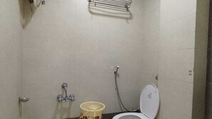 A small bathroom with a toilet, a sink, a shower, and a toilet paper holder. - Lalji S Hotel And Restaurant (Ahmedabad)