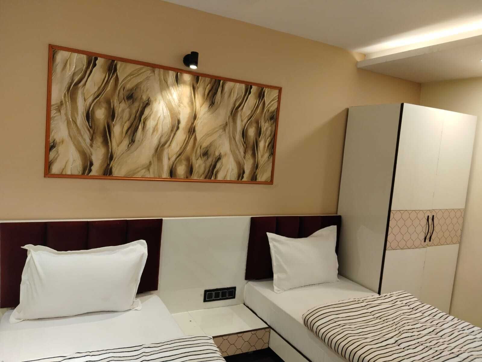 A hotel room with two beds, a wardrobe, a wall-mounted light, and a large abstract painting.
