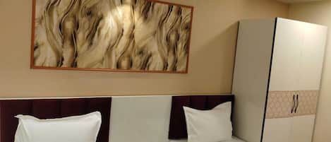 A hotel room with two beds, a wardrobe, a wall-mounted light, and a large abstract painting.