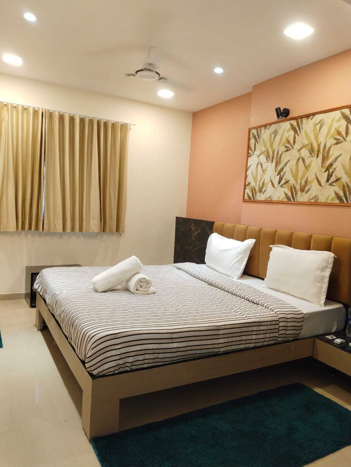 Habitación de hotel con cama, ventilador de techo, luces empotradas, ventana con cortinas y una obra de arte colgada en la pared.