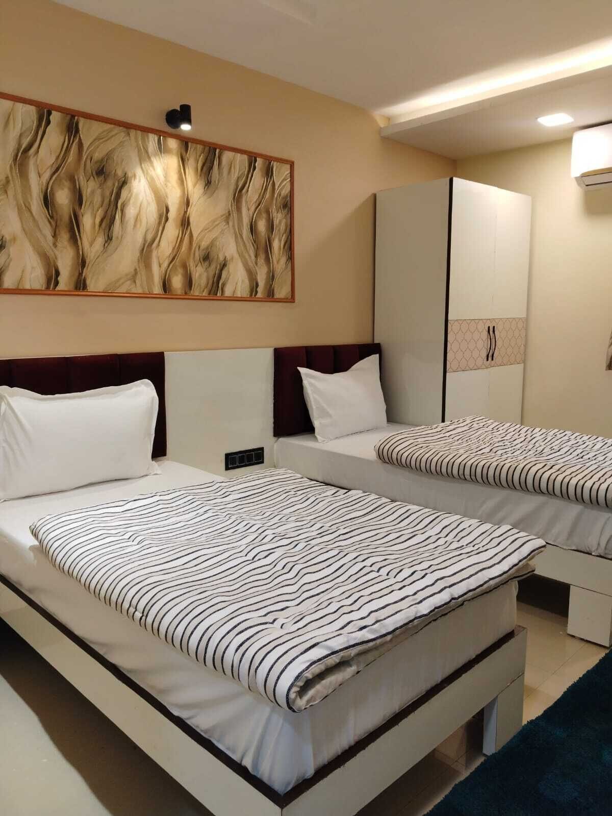 A hotel room with two beds, a large abstract painting on the wall, a wardrobe, and a mirror.