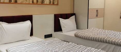 A hotel room with two beds, a large abstract painting on the wall, a wardrobe, and a mirror.