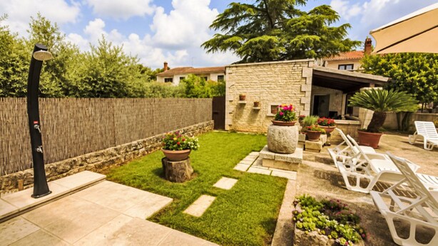Un jardin avec un mur en pierre, une pelouse, des plantes en pot et du mobilier d’extérieur.