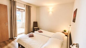 Una camera d'hotel con un letto, una sedia, un tavolino con una pianta e una porta che dà su un balcone.