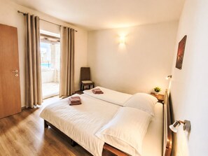 Ein Hotelzimmer mit Bett, Stuhl, kleinem Tisch mit Pflanze und einer Tür zum Balkon.