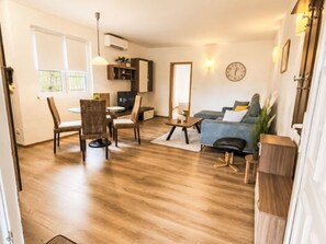 Ein Wohnzimmer mit einer Couch, Sesseln, einem Couchtisch, einem Fernseher und einem Essbereich mit Stühlen und Tisch.