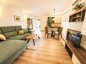 A modern living room with a sofa, coffee table, dining table with chairs, a TV, and a kitchen in the background. - Wohnung mit Schwimmbad by Interhome (Dracevac)