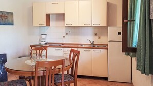 Eine kleine Küche mit Esstisch und Stühlen, einer Kaffeemaschine und einem Kühlschrank.