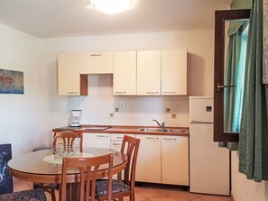 Eine kleine Küche mit Esstisch und Stühlen, einer Kaffeemaschine und einem Kühlschrank.