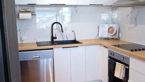 Une cuisine moderne avec des meubles blancs, un lave-vaisselle en acier inoxydable, un évier et une cuisinière.